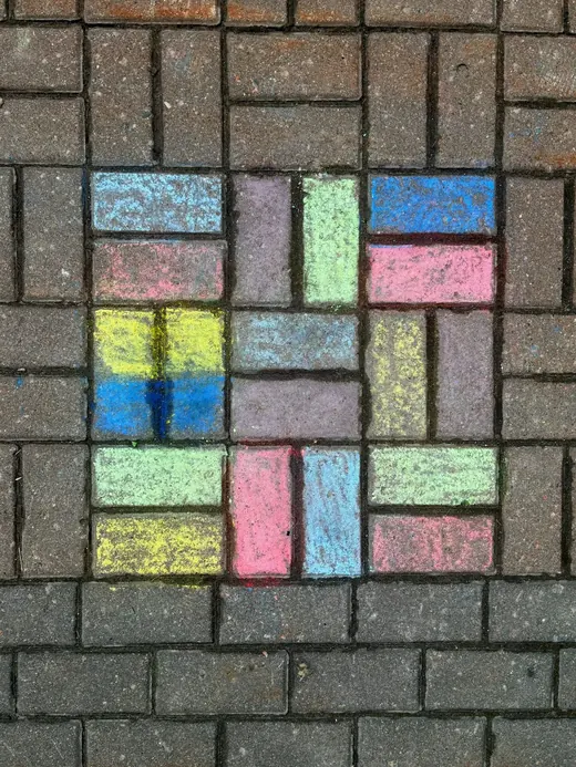 Colorful chalk squares drawn on a brick path, like a hopscotch grid.