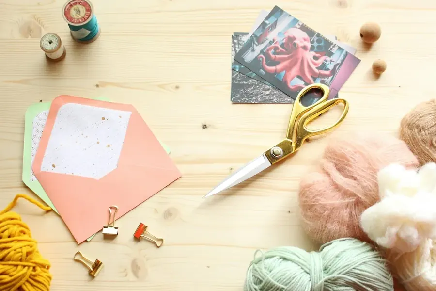 Scissors, envelopes, paper clips and yarn laid out on a light wooden table.